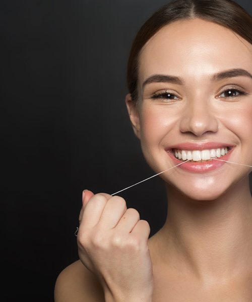 Contented girl is using special interdental thread Portrait of positive young woman who is taking care of her teeth. She is holding dental floss and laughing while looking at camera with joy. Isolated and copy space in left side. Dental health concept